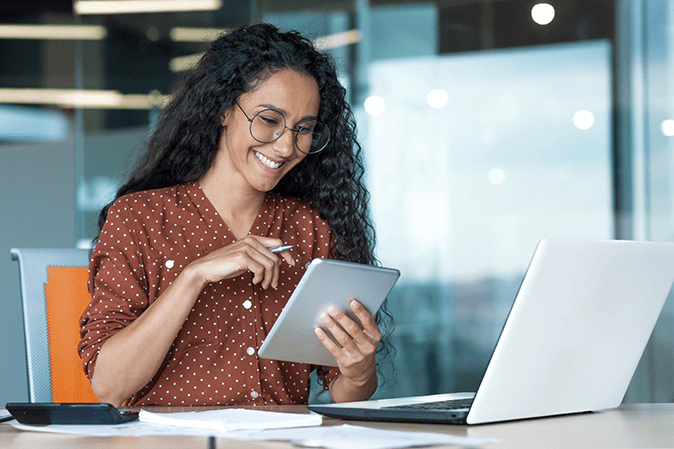 Young beautiful Latin American woman working inside modern office building, paperwork woman uses tablet computer and laptop, accountant calculates reports and accounts, financial documents.