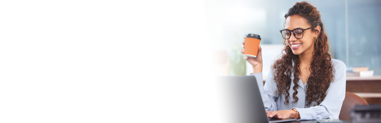 Young woman smiling while holding a coffee working on her laptop